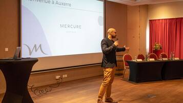 Presentación en una sala de conferencias con una pantalla que muestra 'Bienvenue à Auxerre' y 'MERCURE HOTELS'.