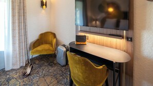 A hotel room with a flat-screen TV mounted on the wall, a desk with a chair, a suitcase, and a pair of shoes on the floor. - Mercure Auxerre Autoroute du Soleil (Appoigny)