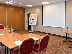Un salón de conferencias con una larga mesa, sillas, un proyector y una pantalla.