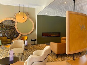 A modern lobby with a fireplace, seating area, and a decorative wall with circular patterns. - Mercure Auxerre Autoroute du Soleil (Appoigny)