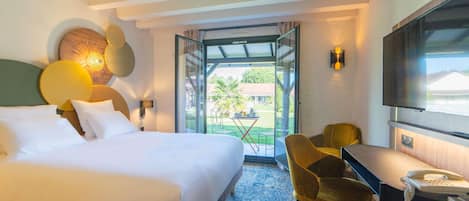 Habitación de hotel con cama, escritorio, silla, televisor y puerta de vidrio que da a un espacio exterior.