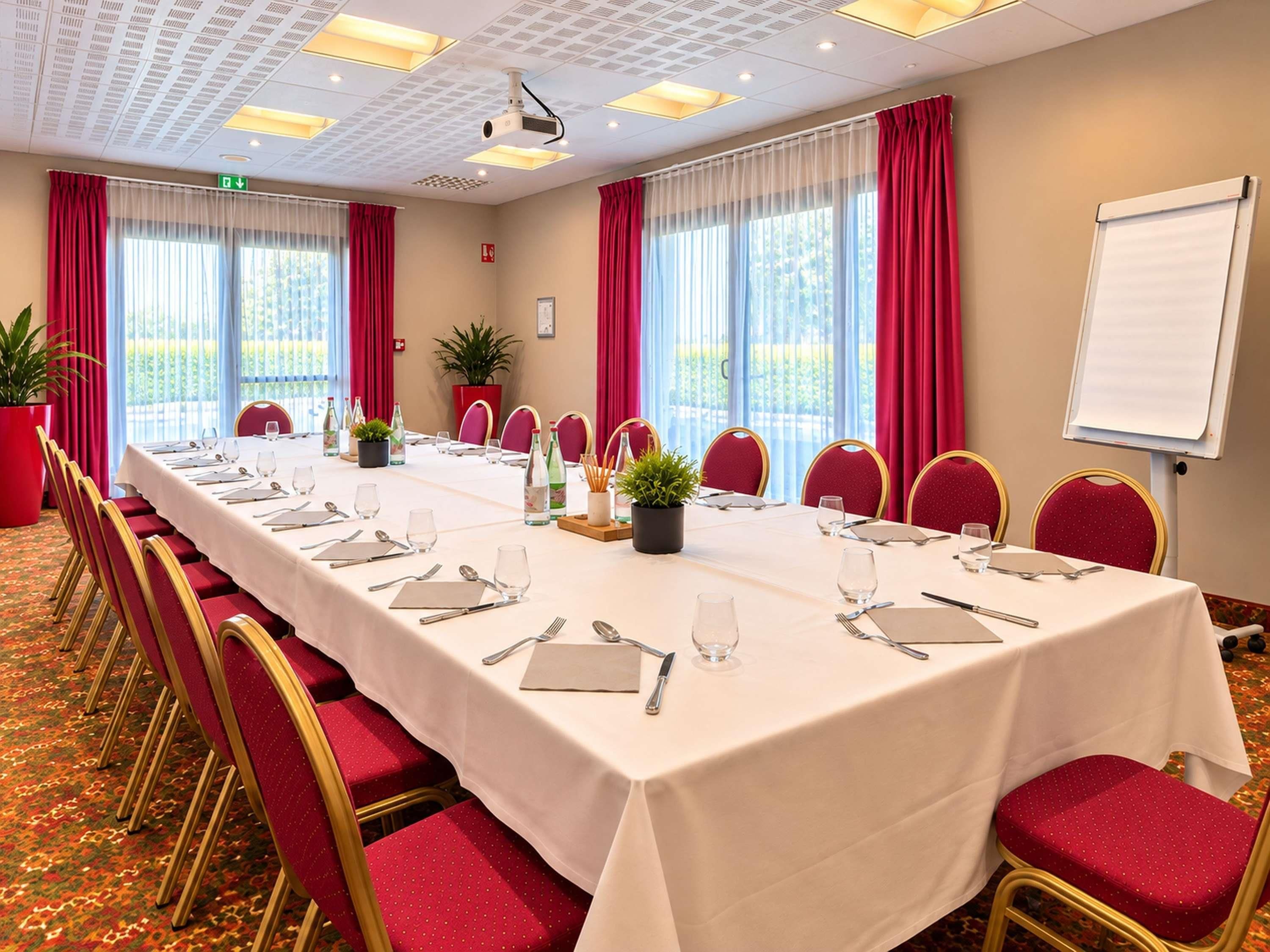 A conference room with a long table set for a meeting, red chairs, a projector, and a whiteboard.
