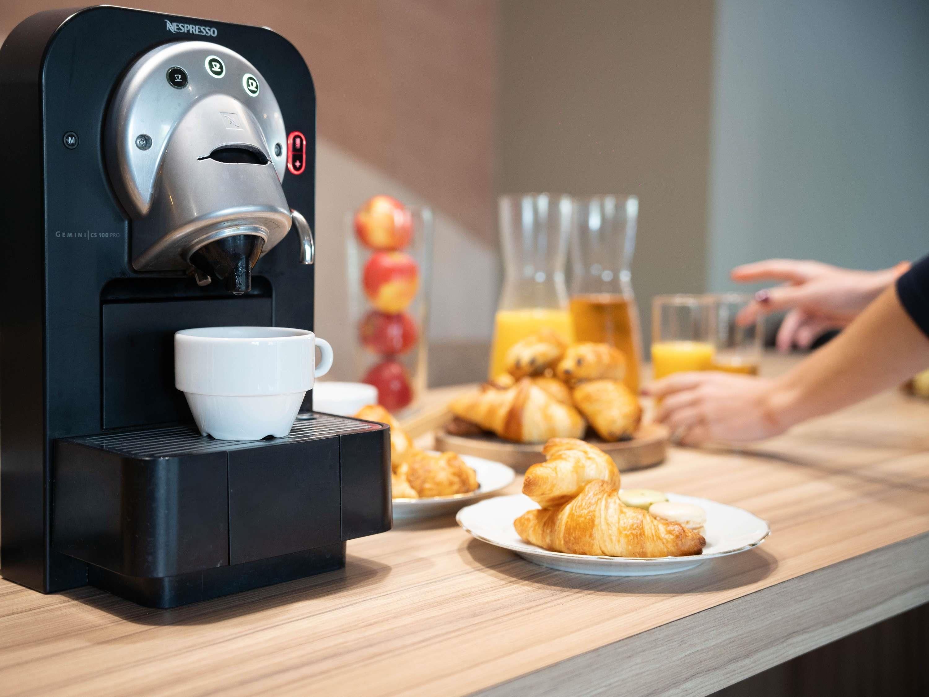 A coffee machine with a cup, croissants, and a glass of orange juice on a wooden table.