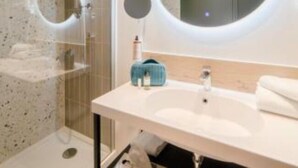 A modern bathroom with a glass shower enclosure, a round mirror, a white sink, and a towel rack. - Mercure Auxerre Autoroute du Soleil (Appoigny)