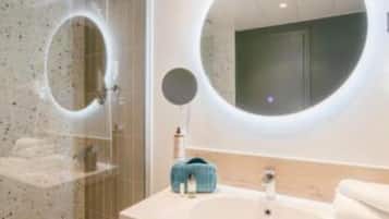A modern bathroom with a glass shower enclosure, a round mirror, a white sink, and a towel rack.