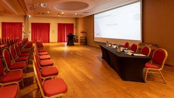 Un salón de conferencias con filas de sillas rojas, una mesa negra y una pantalla de proyector mostrando 'MERCURE HOTELS'.