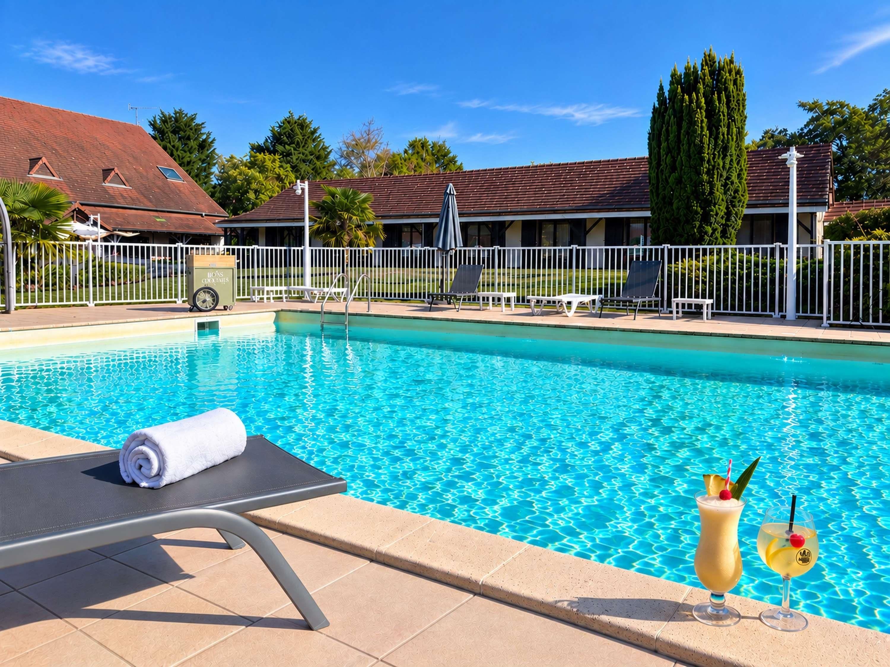 Piscina con sillas de descanso y una toalla, rodeada de una valla y follaje.