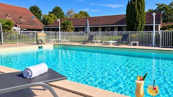 Piscina con sillas de descanso y una toalla, rodeada de una valla y follaje.