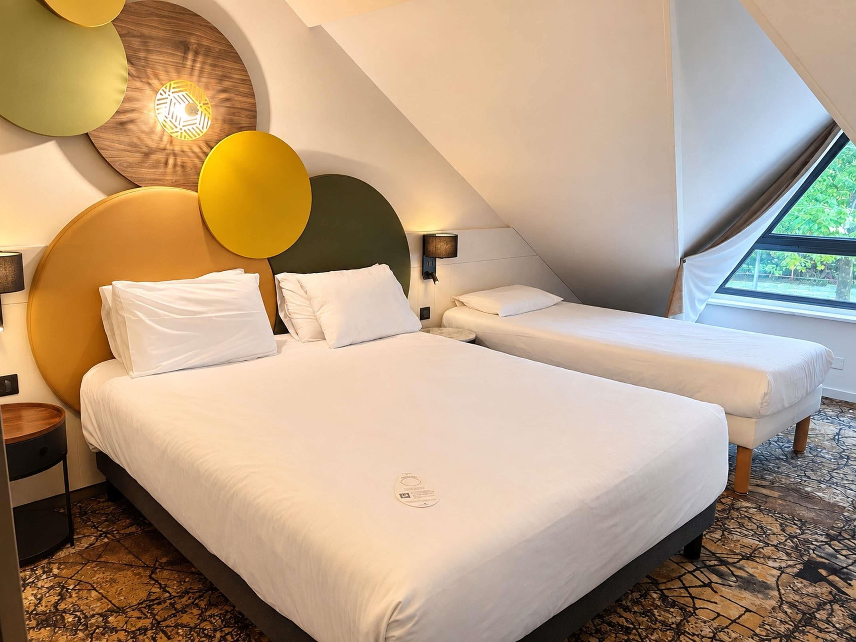 A hotel room with two beds, a large window, and a unique ceiling design.