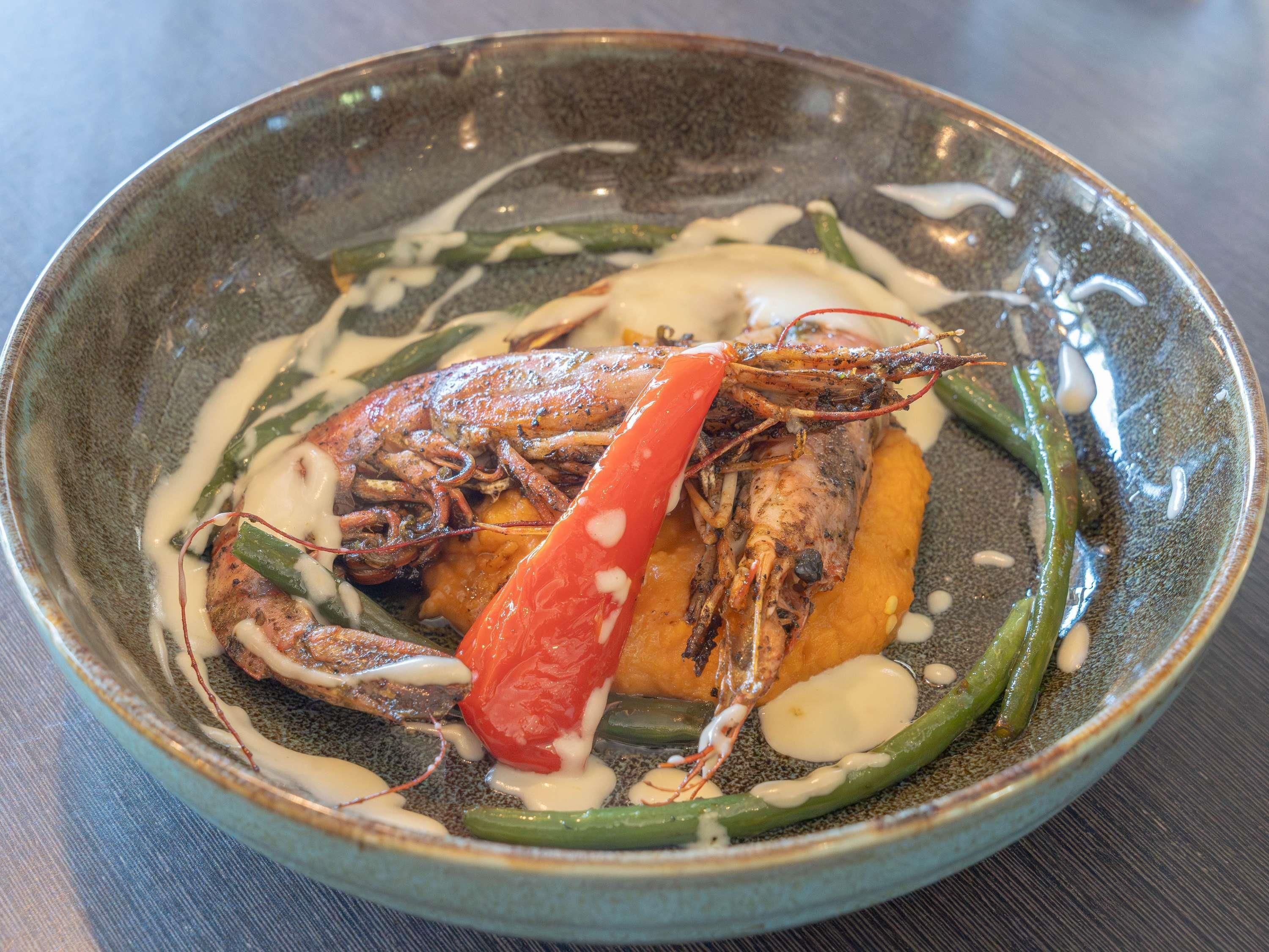 A bowl of seafood dish with a lobster tail, green beans, and a red chili pepper.
