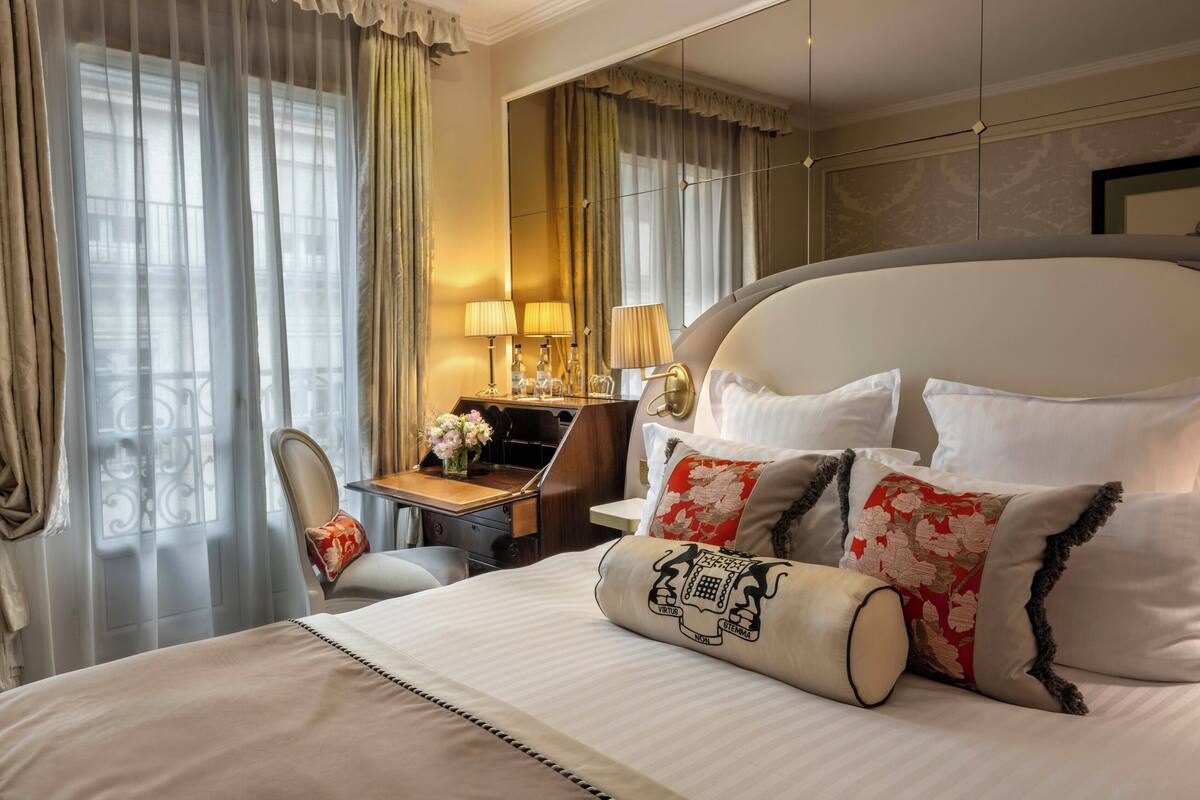 A hotel room with a large bed, a desk with a lamp, and a chair.