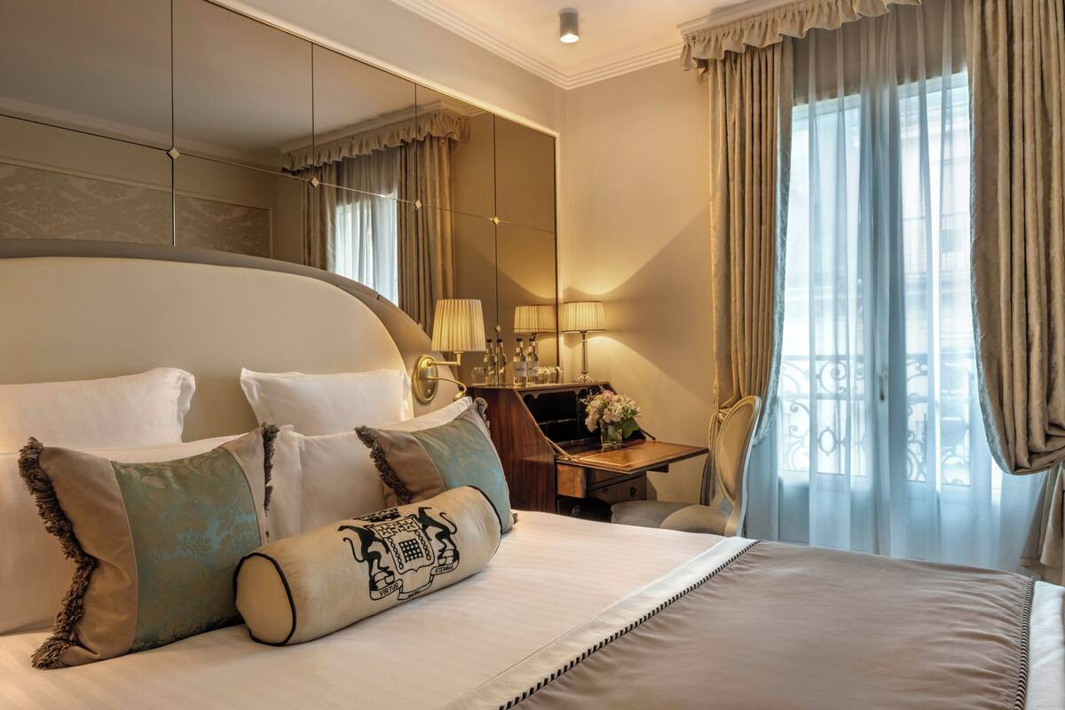 A hotel room with a large bed, a desk with a lamp, and a view of the outdoors.