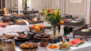 Ein Buffet mit verschiedenen Speisen, darunter Obst, Gebäck und eine Torte auf einer weißen Tischdecke.