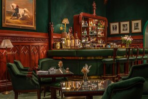 A bar area with green upholstered seating, a bar counter with bottles, and framed pictures on the wall. - Hôtel Westminster (Paris)