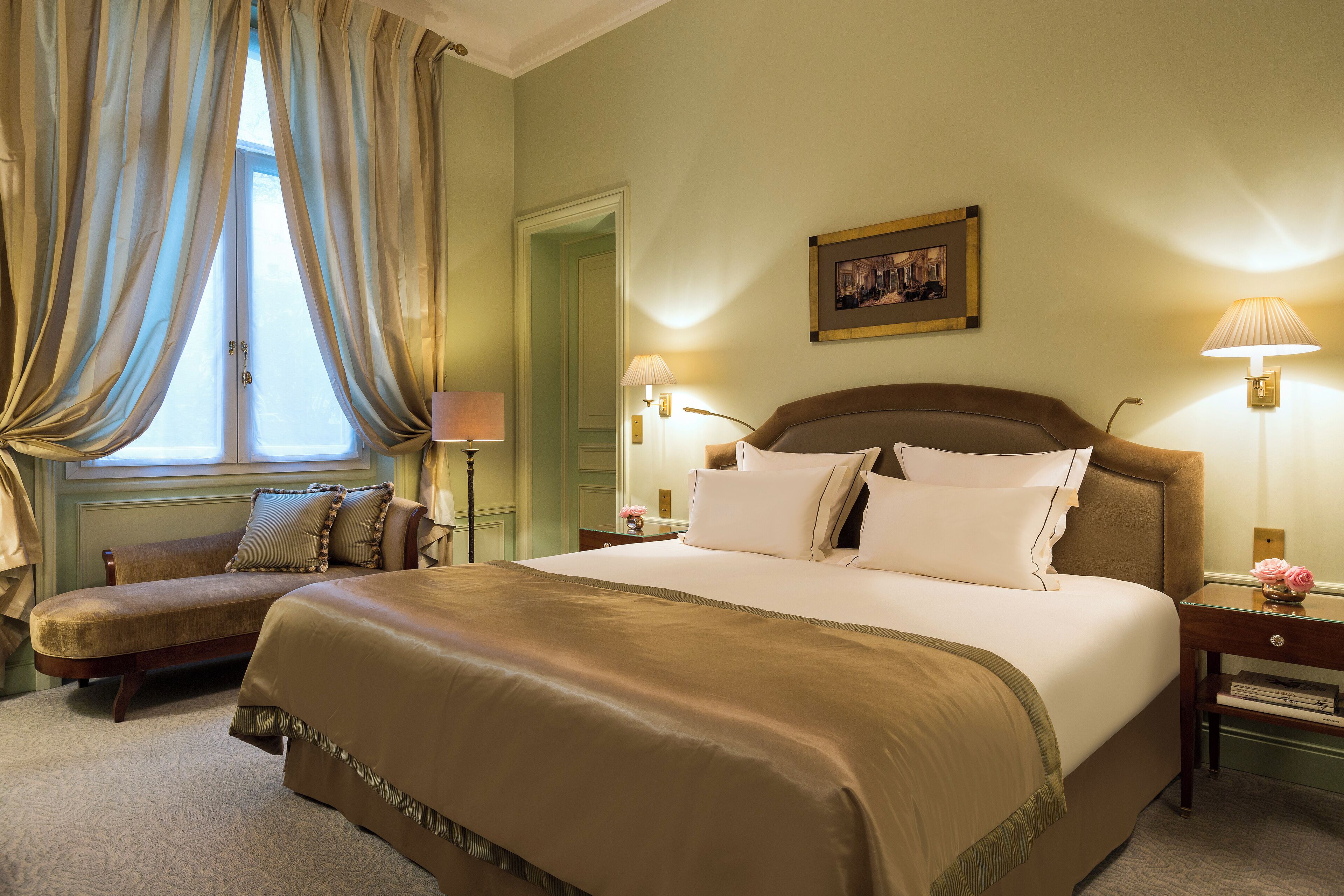 A hotel room with a large bed, two bedside tables with lamps, a chair, and a window with curtains.