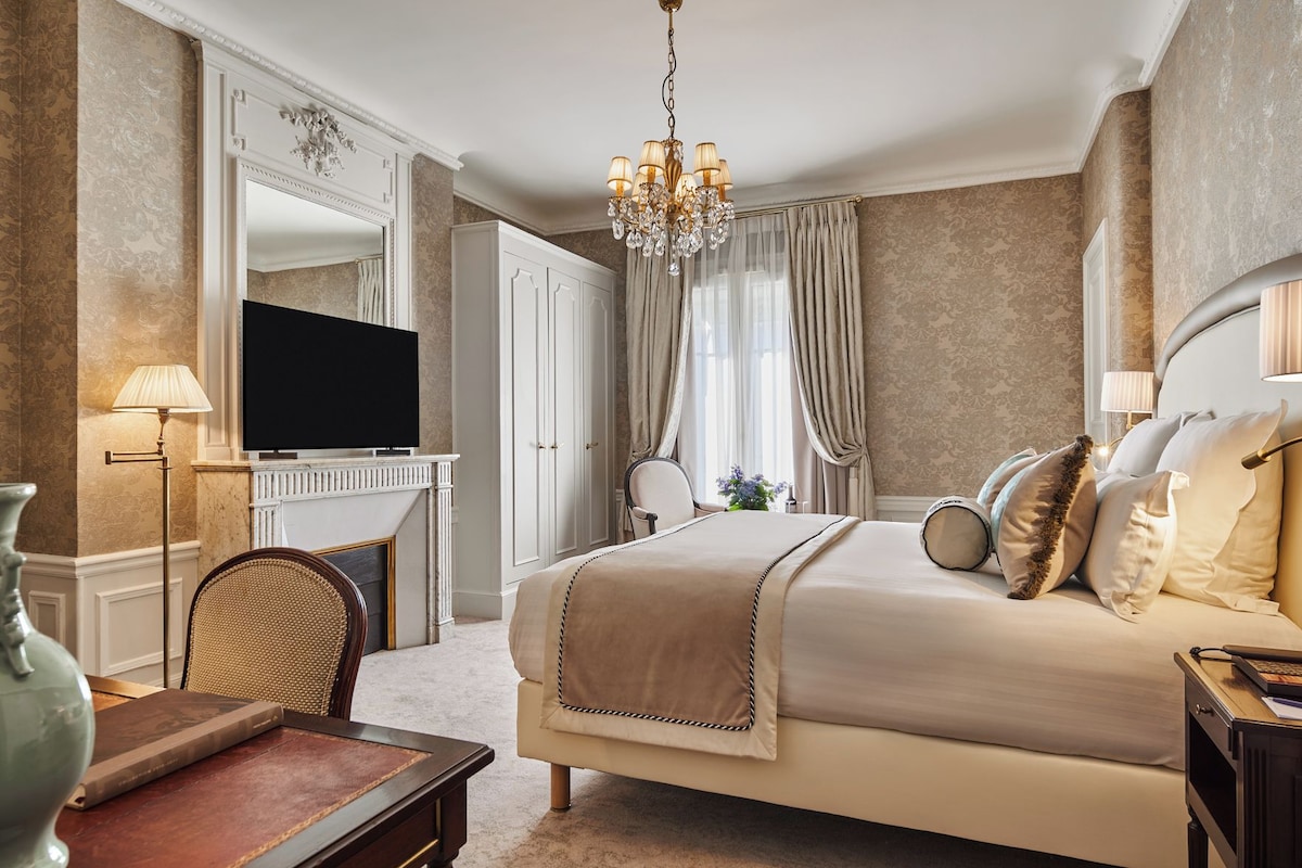 Una habitación de hotel con una cama grande, televisión, candelabro y escritorio con lámpara.