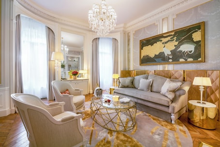 A luxurious living room with a sofa, armchairs, a glass coffee table, and a chandelier.