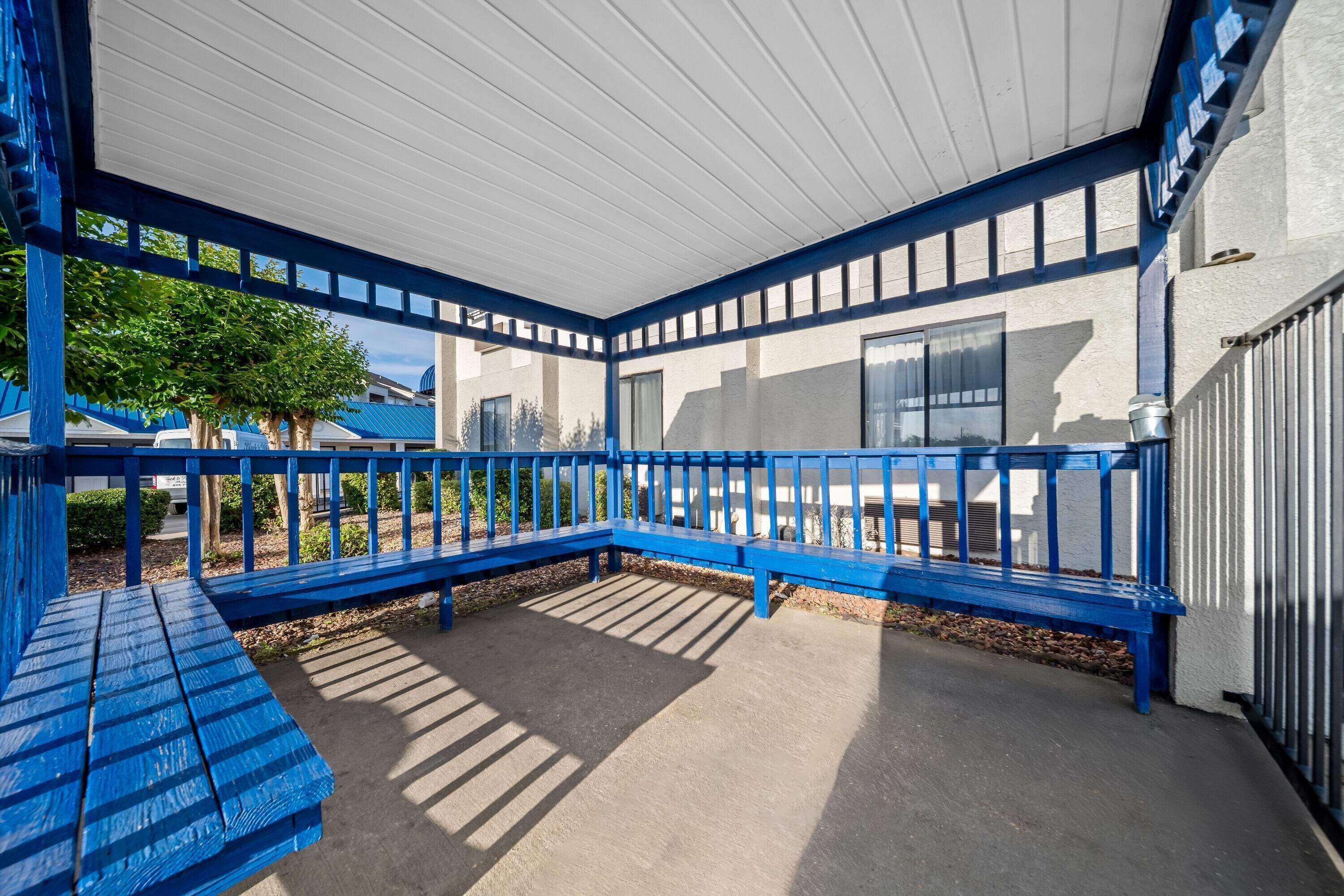 Un espace extérieur abrité, doté de rampes et de bancs bleus, d’un sol en béton et offrant une vue sur un bâtiment avec des fenêtres.