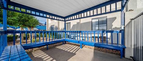 Un espace extérieur abrité, doté de rampes et de bancs bleus, d’un sol en béton et offrant une vue sur un bâtiment avec des fenêtres.