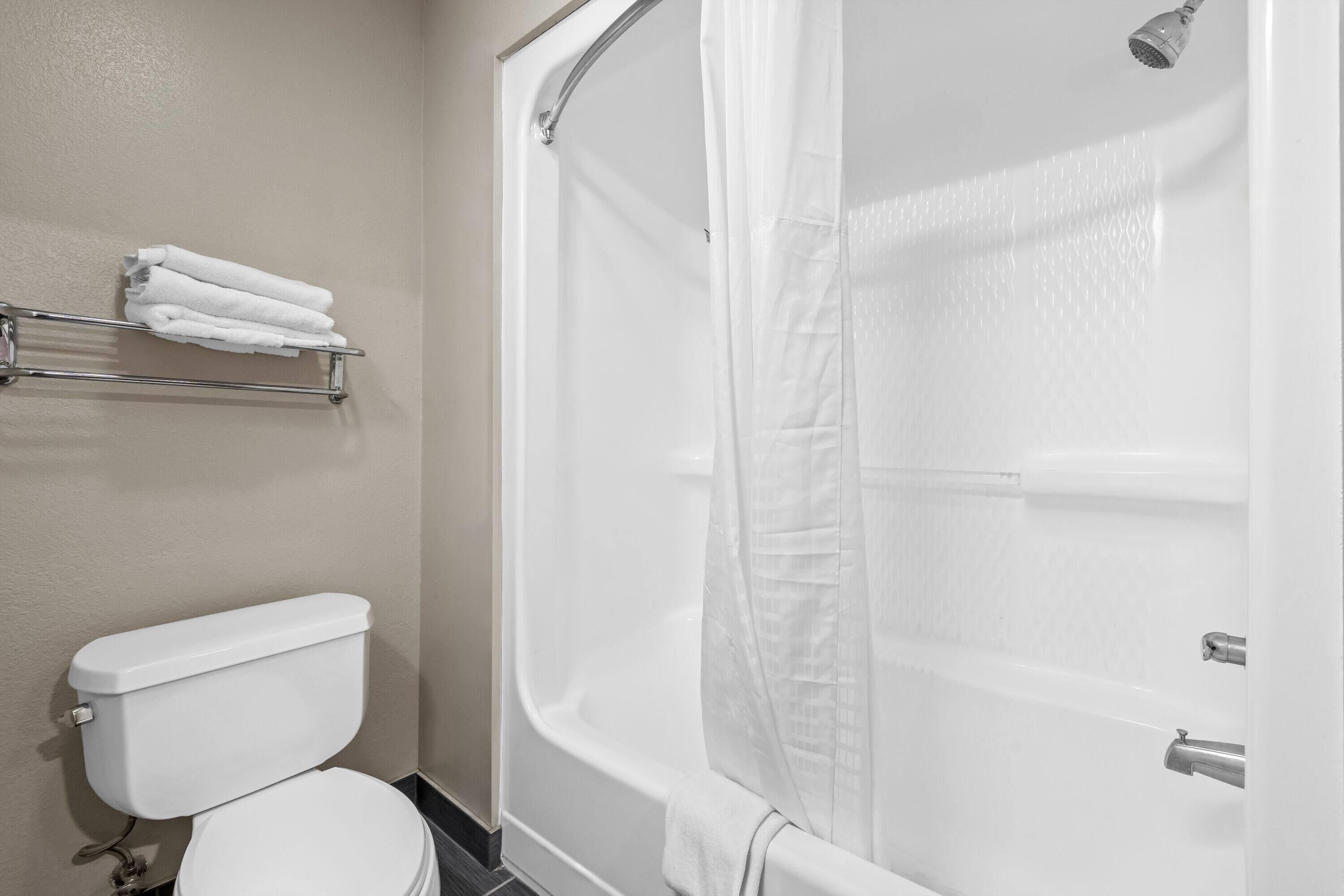 A bathroom with a white toilet, a shower with a white curtain, and a towel rack with folded towels.
