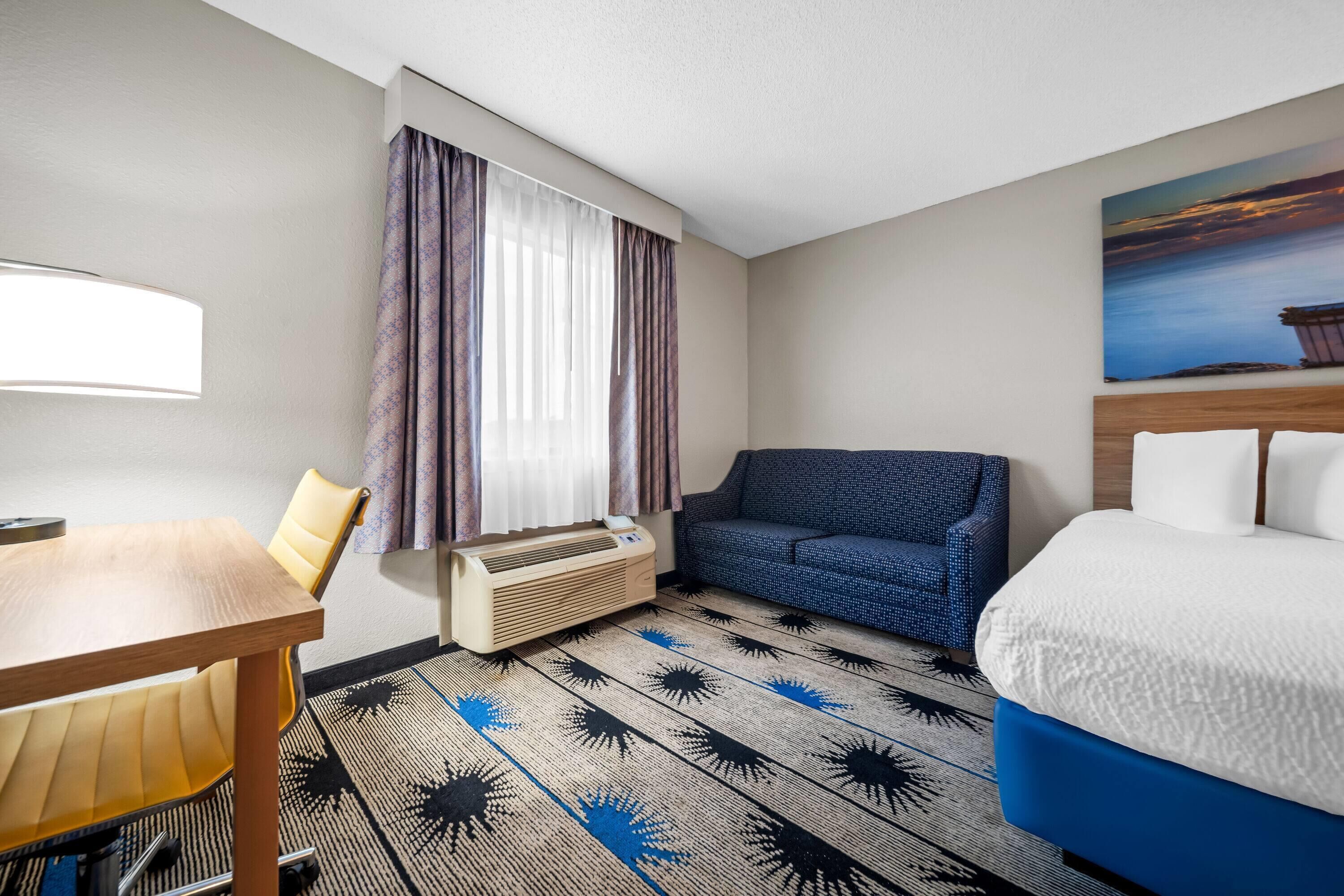 A hotel room with a bed, a sofa, a table, and a window with curtains.