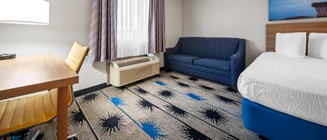 A hotel room with a bed, a sofa, a table, and a window with curtains.