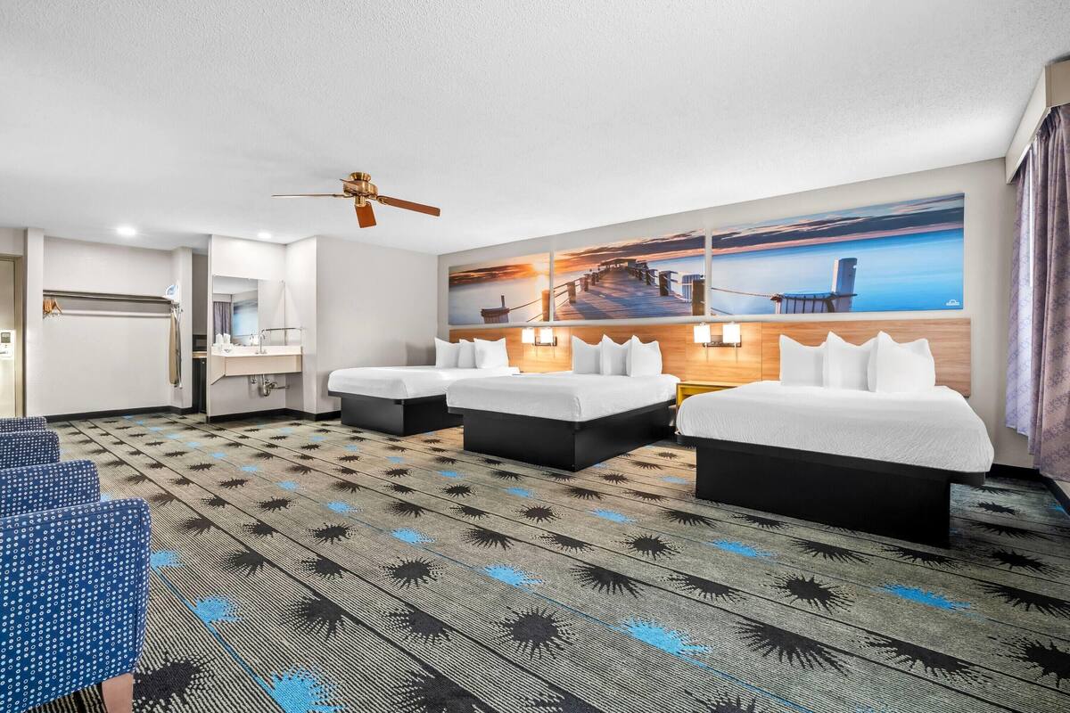 A hotel room with two beds, a desk, a chair, a large painting, and a patterned carpet.