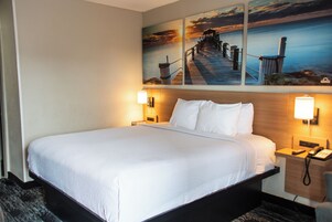Habitación de hotel con una cama grande, dos mesitas de noche y un cuadro que muestra un muelle y una puesta de sol.