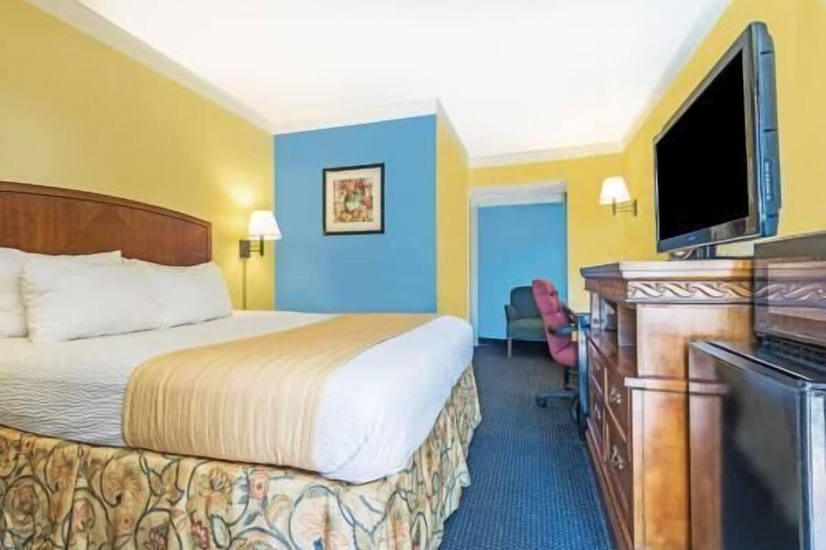 A hotel room with a bed, a desk with a television, a chair, and a painting on the wall.