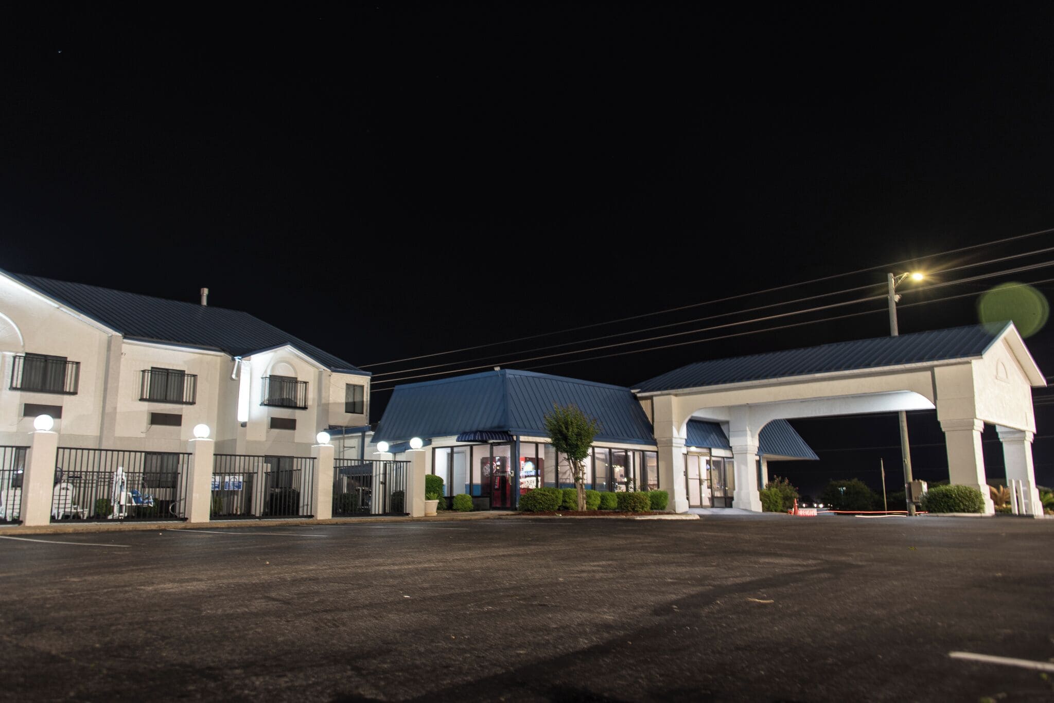 A hotel with a covered outdoor area, a parking lot, and a gated entrance.