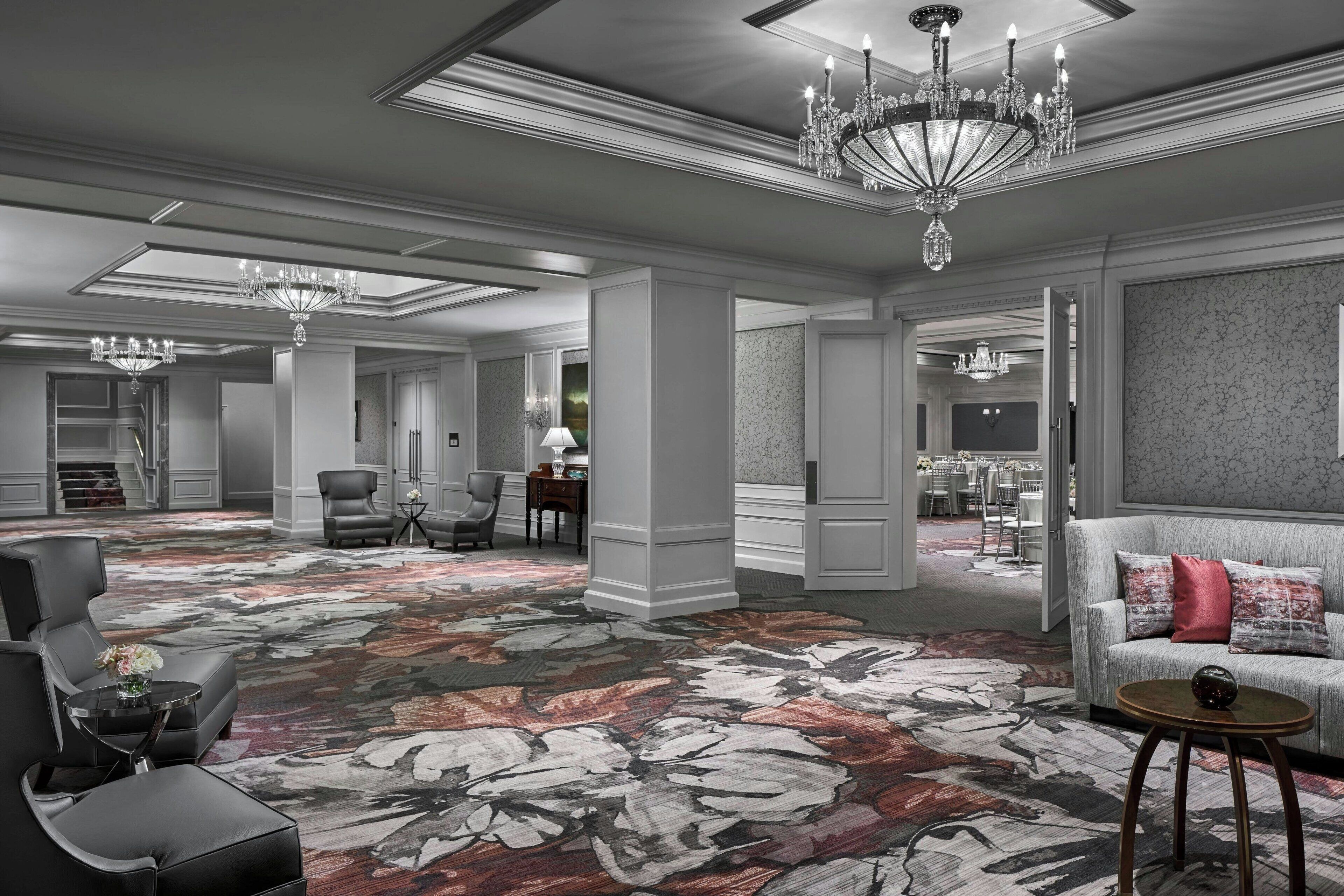 Un amplio vestíbulo de hotel con una alfombra floral grande, varias zonas de estar y un gran candelabro.