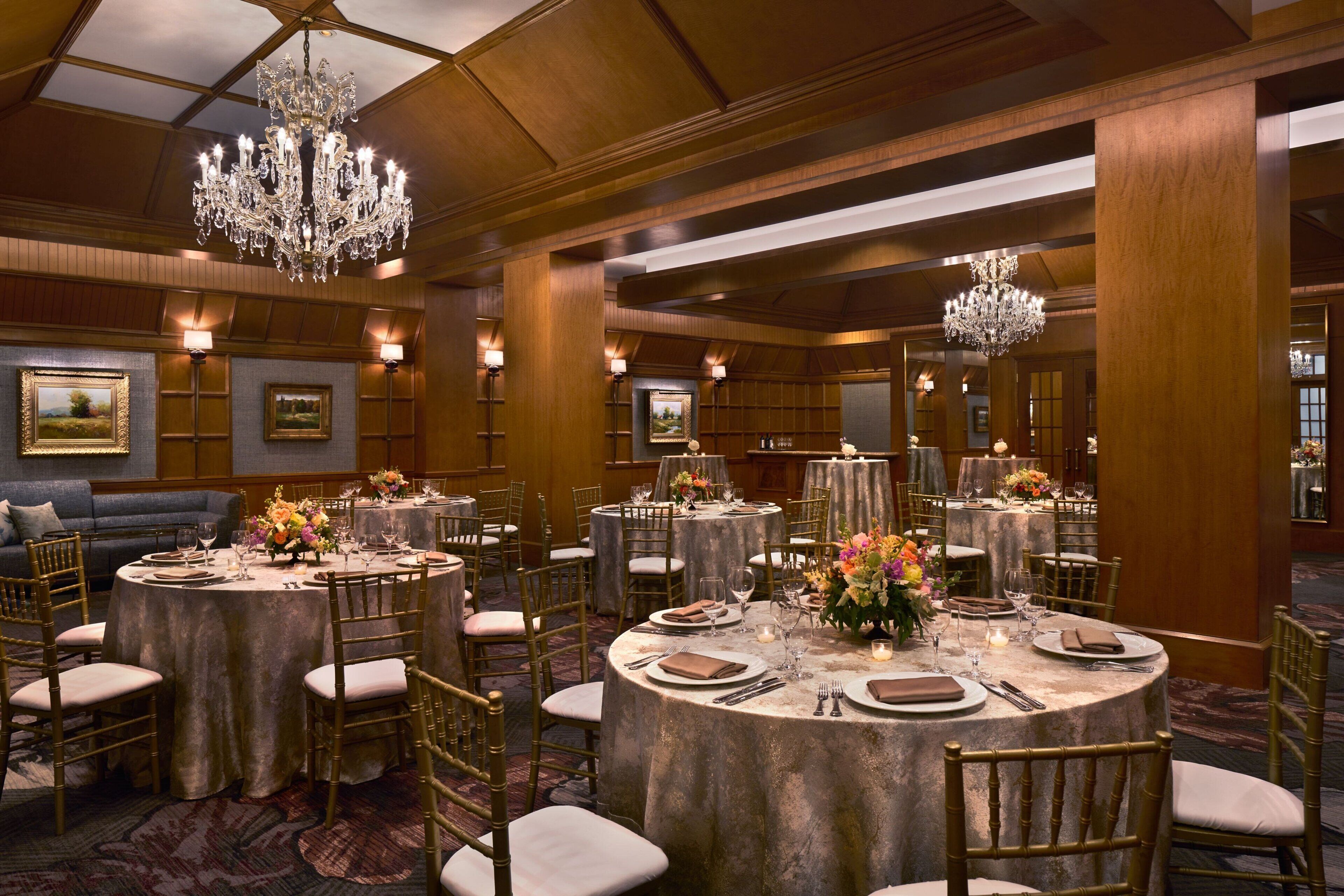 Un salón de banquetes con mesas redondas, sillas doradas, candelabros y obras de arte enmarcadas en las paredes.