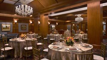 Un salón de banquetes con mesas redondas, sillas doradas, candelabros y obras de arte enmarcadas en las paredes.