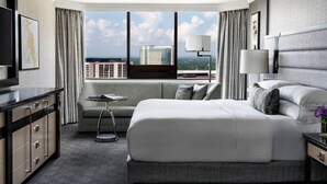 Une chambre d’hôtel moderne dotée d’un grand lit, d’un canapé, d’un bureau et offrant une vue sur le paysage urbain grâce à de grandes fenêtres.