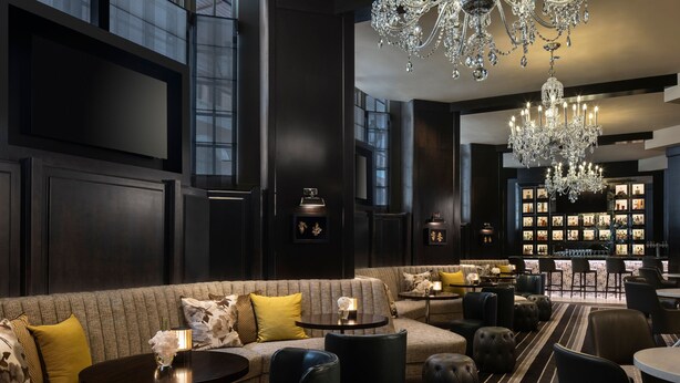 Un espace de détente moderne comprenant un canapé, des fauteuils et un coin bar agrémenté d’un lustre.