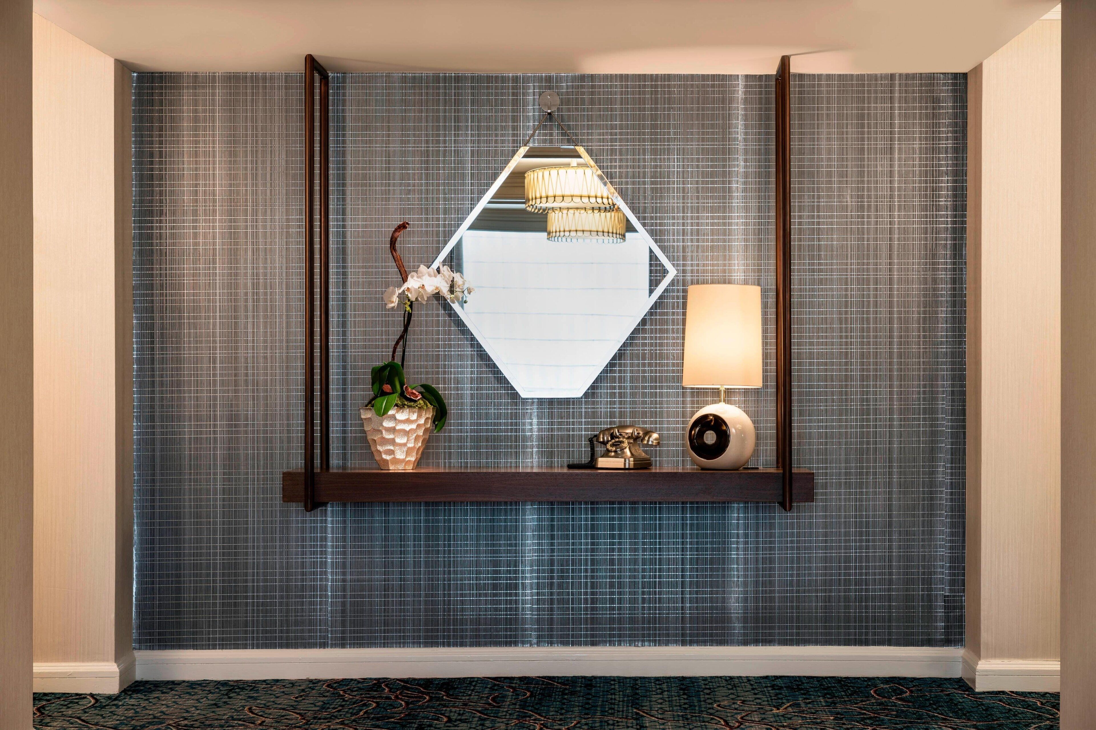 A room with a mirrored wall, a wooden shelf with decorative items, a lamp, and a wall-mounted light fixture.
