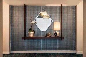 A room with a mirrored wall, a wooden shelf with decorative items, a lamp, and a wall-mounted light fixture.