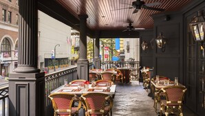 Un café en plein air avec des tables et des chaises en osier, un plafond en bois et une vue sur la rue.