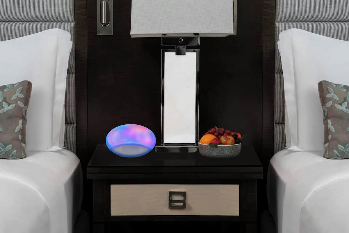 A modern bedroom with a nightstand, a lamp, a mirror, and a bowl of fruit.
