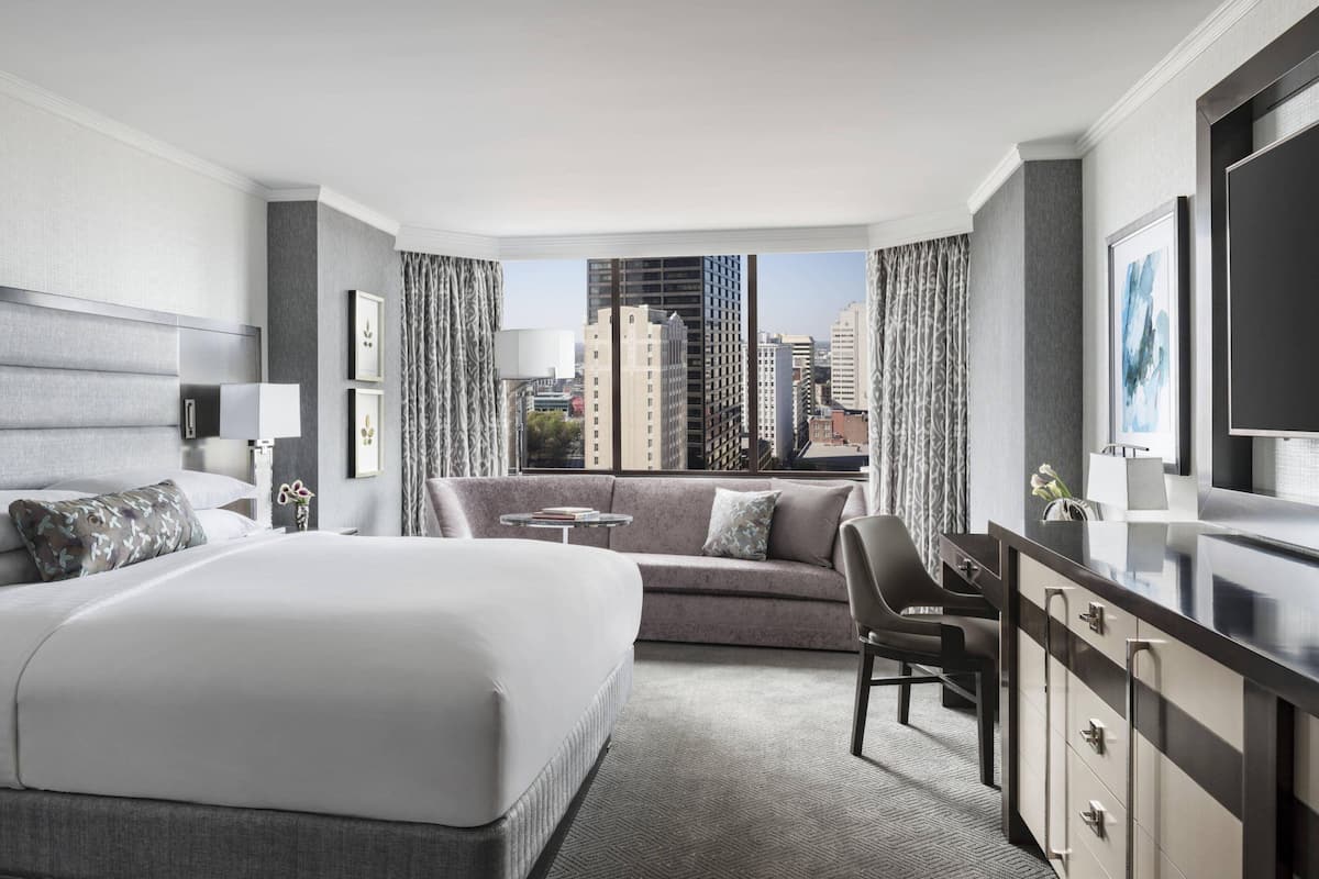A modern hotel room with a large bed, a sofa, a desk, and a view of the cityscape.