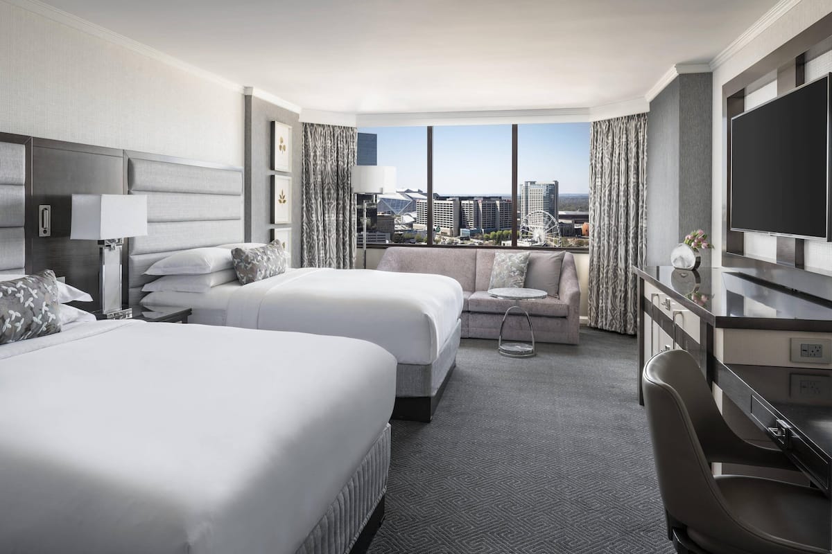A hotel room with two beds, a sofa, a TV, and a view of the cityscape.