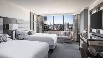 A hotel room with two beds, a sofa, a TV, and a view of the cityscape.