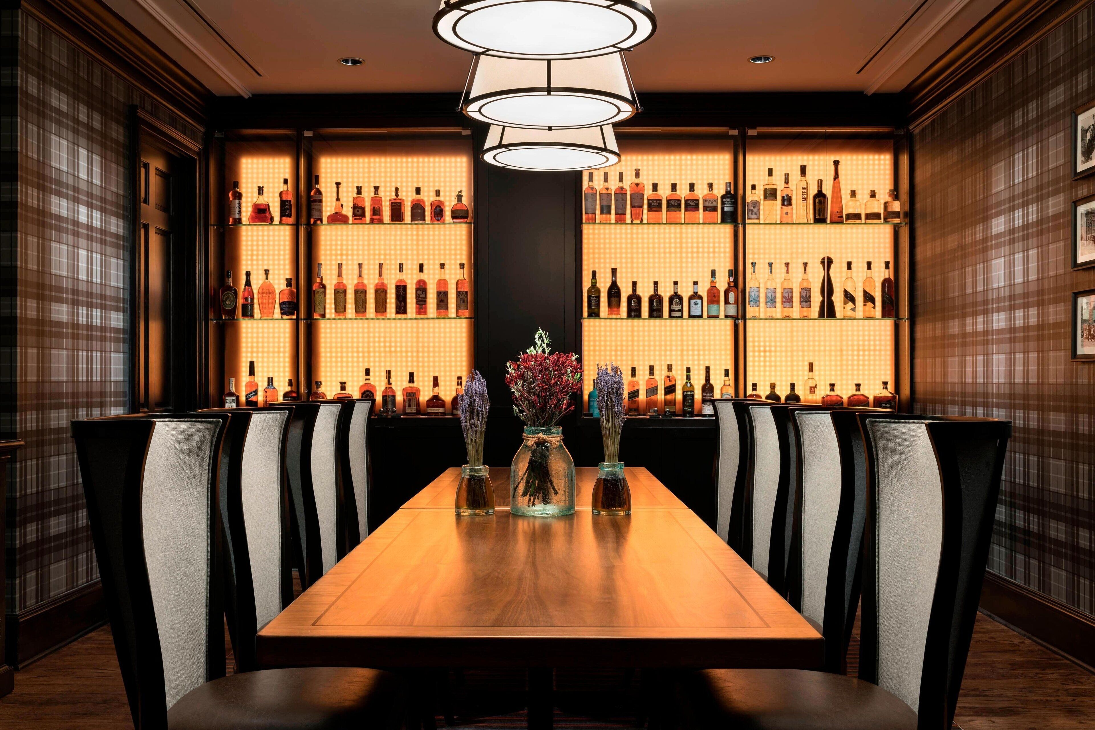 Un restaurante con una larga mesa de madera, varias sillas y una pared llena de botellas de licores.