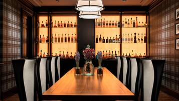 Un restaurante con una larga mesa de madera, varias sillas y una pared llena de botellas de licores.
