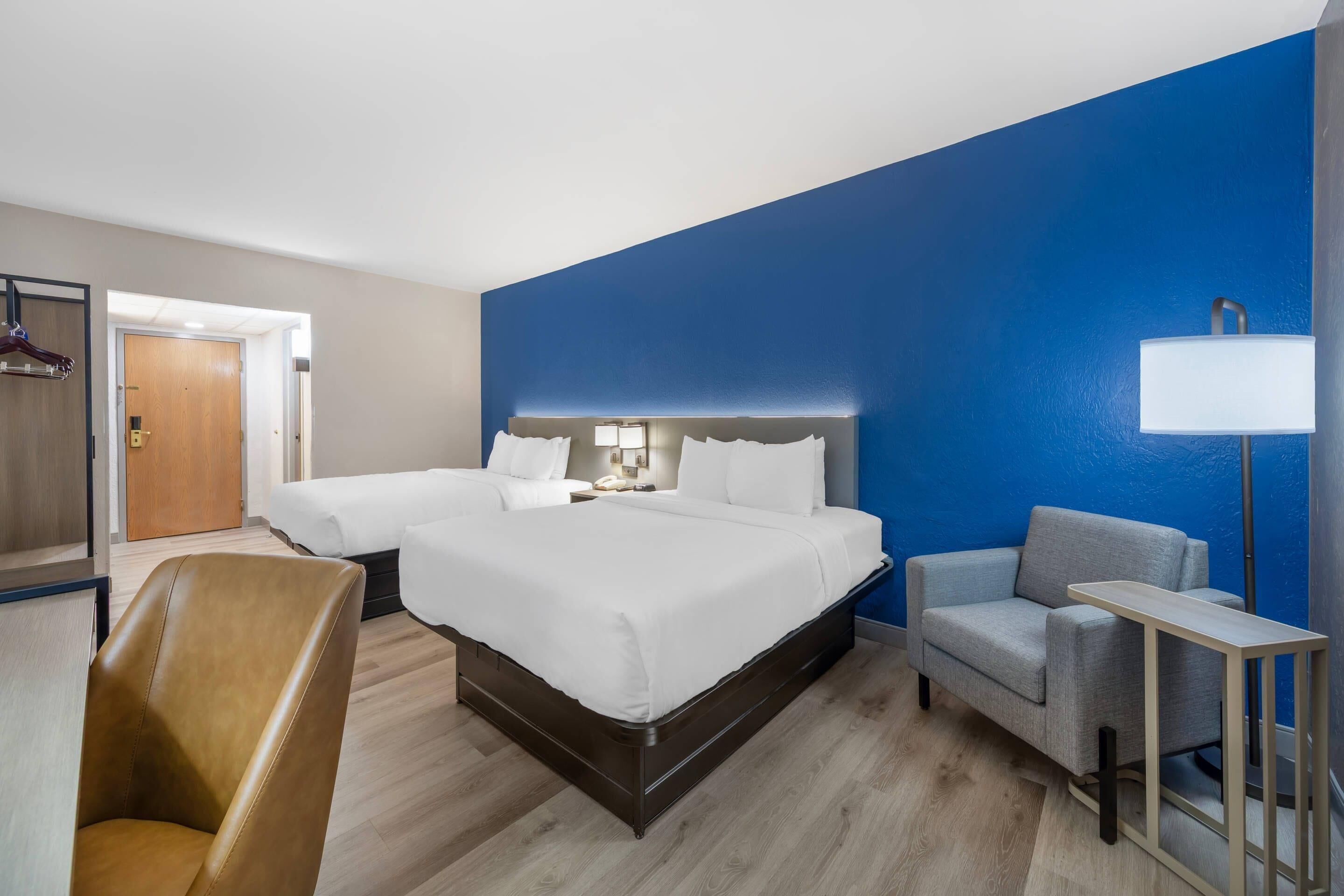 Une chambre d’hôtel avec un grand lit, deux tables de chevet, une chaise, un bureau et une armoire.