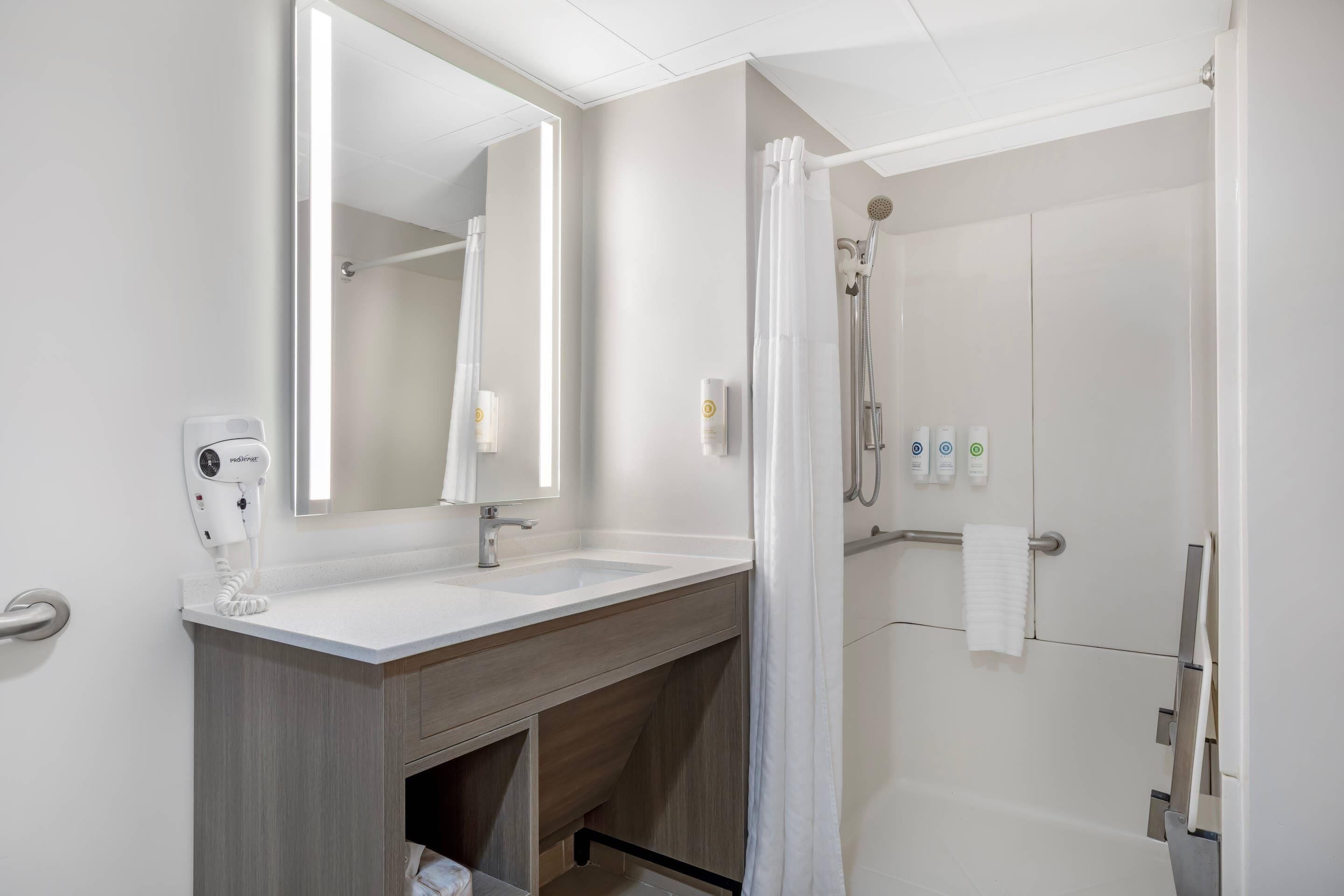 A modern bathroom with a vanity, mirror, shower, and towel rack.