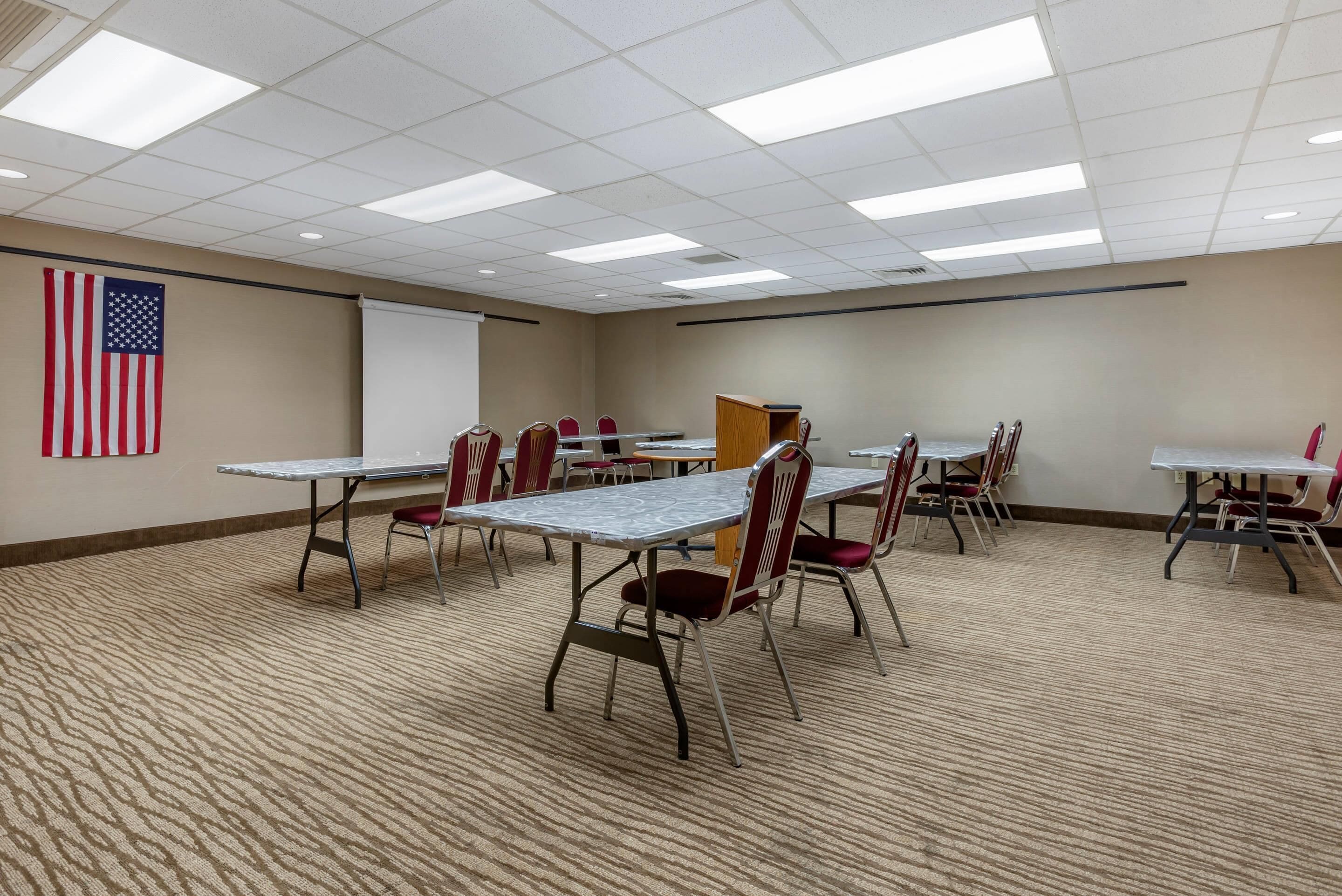 A conference room with tables, chairs, a projector screen, and an American flag.
