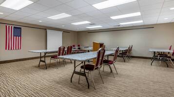 A conference room with tables, chairs, a projector screen, and an American flag.