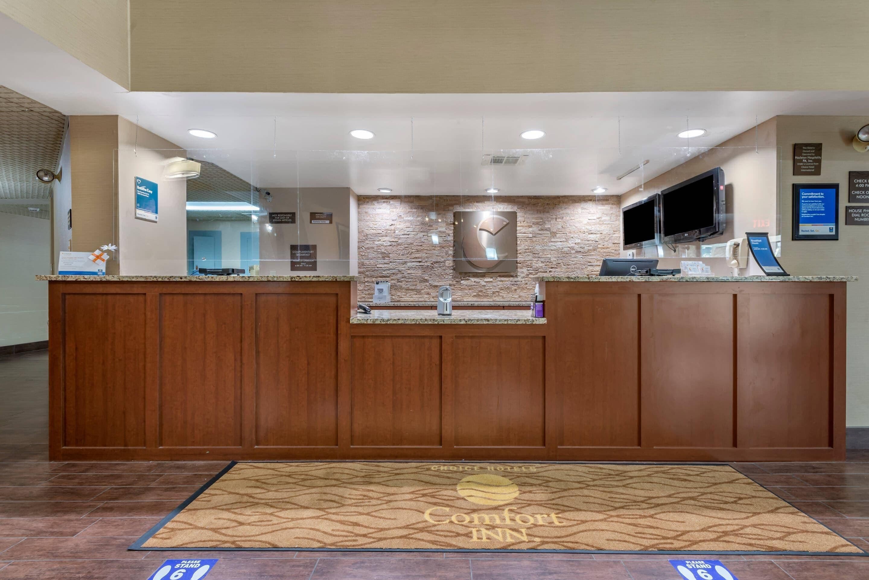 A hotel reception desk with a stone wall backdrop, a flat-screen TV, and a digital display.