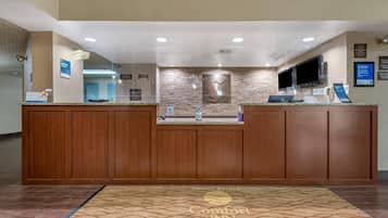 A hotel reception desk with a stone wall backdrop, a flat-screen TV, and a digital display.